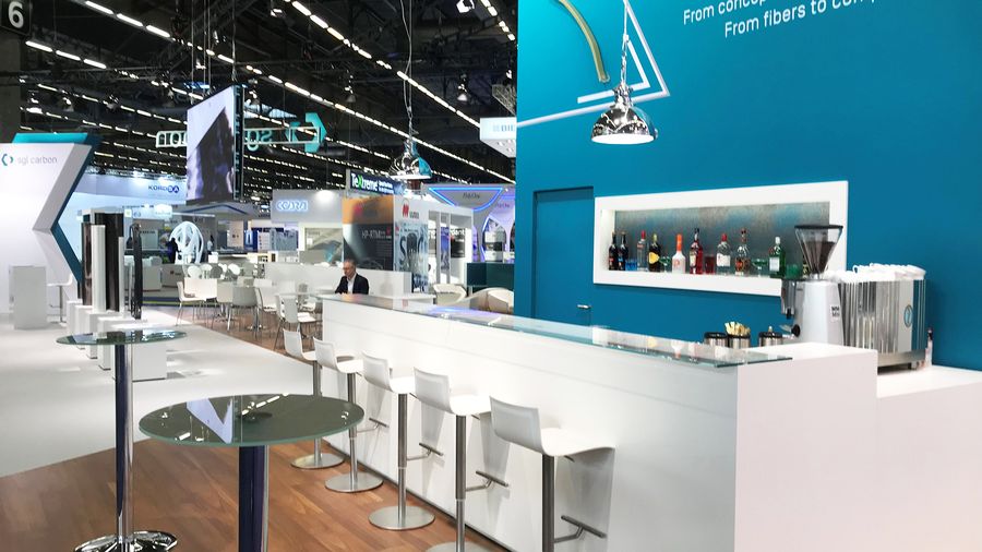 Lange weiße Theke mit Barhockern auf einem Messestand, dahinter eine Servicekraft an der Espressomaschine
