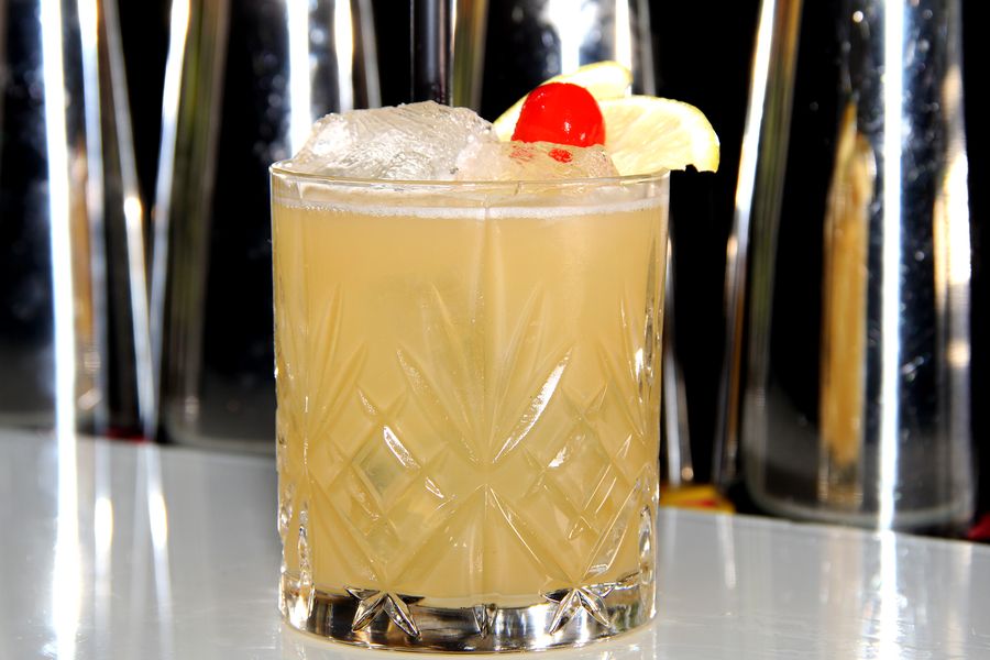 Heller Sour im Kristallglas mit Crushed Ice, Cocktailkirsche und Ananasscheibe auf der Bartheke