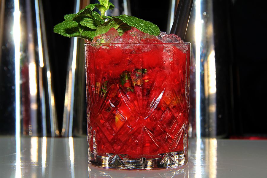 Roter Beerencocktail im geschliffenen Kristallglas mit frischer Minze, im Hintergrund die beleuchtete Bar