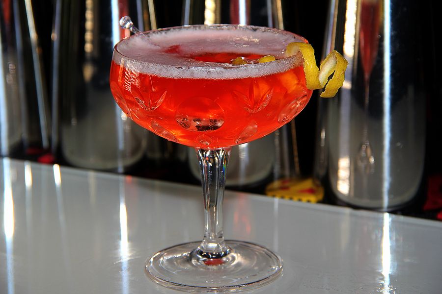 Roter Cocktail in einer Coupette mit Zuckerrand und Zitronenzeste auf der Bartheke