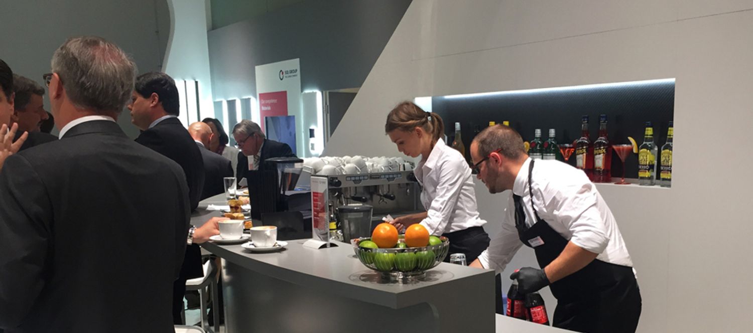Servicekräfte bedienen Messebesucher an der Kaffee- und Cocktailtheke eines Messestands