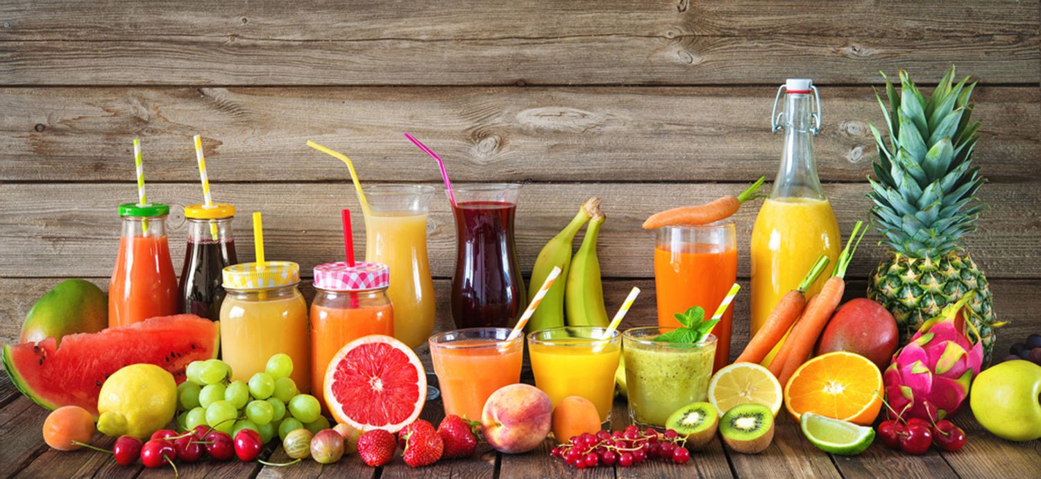 Frisch gepresste Säfte und Smoothies in Flaschen und Gläsern vor einer Holzwand, umgeben von Obst