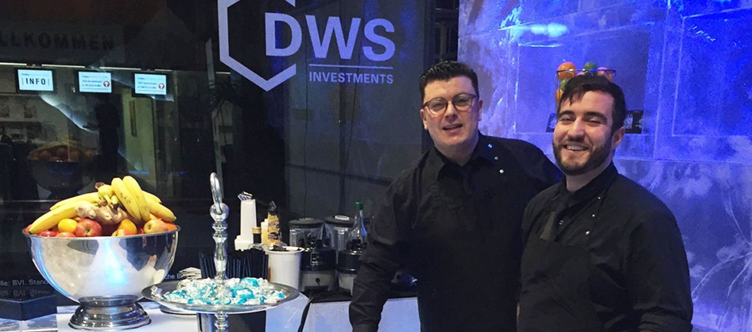 Zwei Barkeeper von barmotion an einer blau beleuchteten Eisbar auf einem Messestand