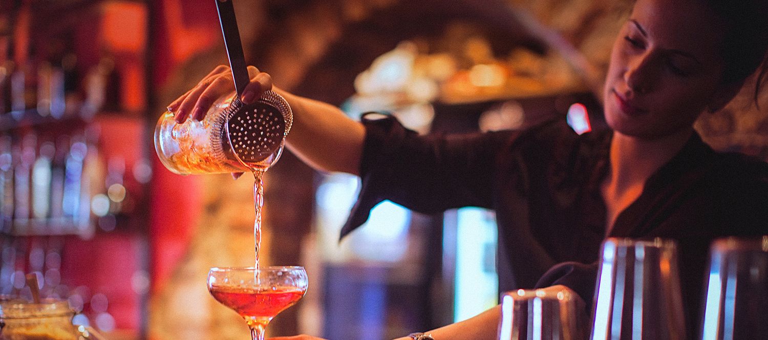 Barkeeperin seiht einen Cocktail durch ein Barsieb in eine Coupette-Schale