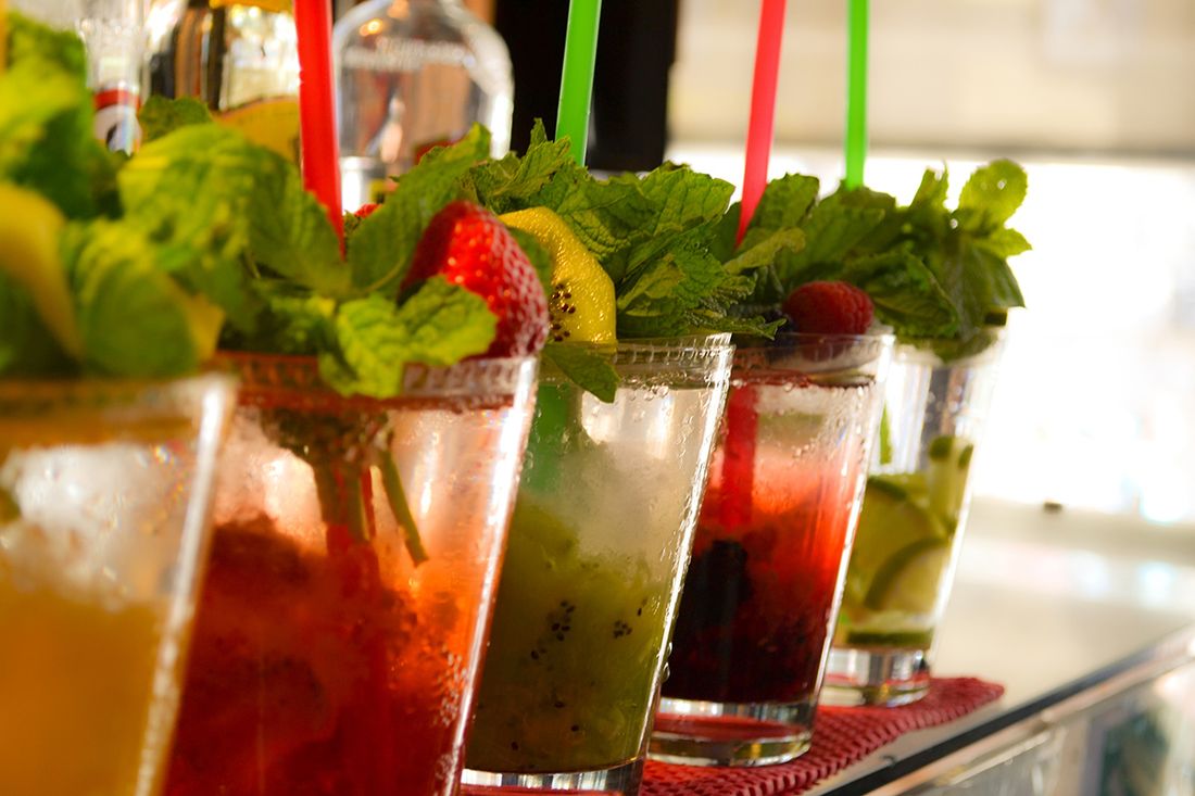 Bunte Fruchtdrinks mit frischer Minze, Limette und Beeren, aufgereiht auf der Bartheke