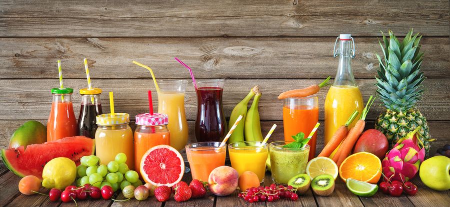 Frisch gepresste Säfte und Smoothies in Gläsern und Flaschen, umgeben von Obst und Gemüse